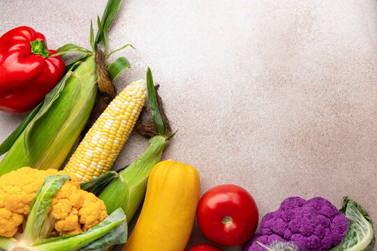 Fresh vegetables including corn and peppers arranged on a light stone background with copy space