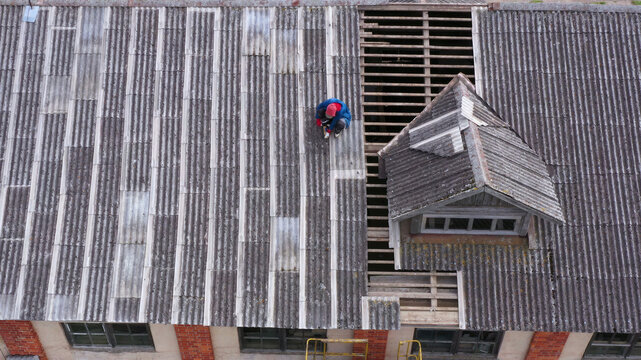 Aerial view of a worker repairing a corrugated roof on a building in Latvija.