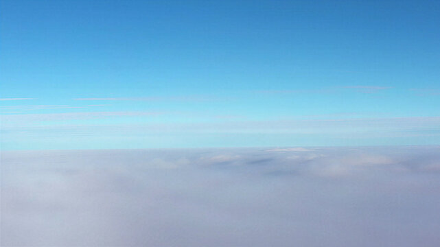 Aerial view of a thick layer of clouds stretching to the horizon under a clear blue sky in Latvija.