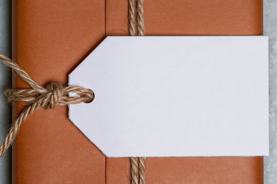 Blank gift tag tied with jute twine on a kraft paper wrapped parcel, featuring a textured matte finish for a craft mockup with copy space