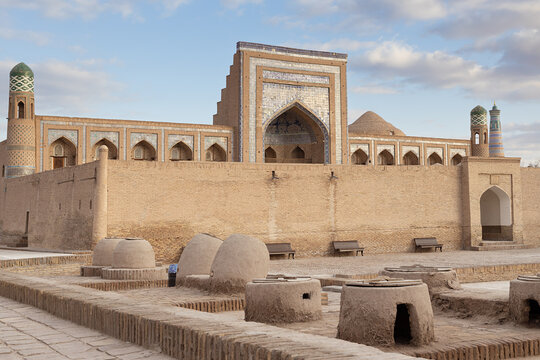 Muhammad Rahim Khan Madrasah in Ichan Kala with traditional clay tandoor ovens in the foreground courtyard. Historic Khiva landmark in Uzbekistan, ideal for travel publications and cultural heritage.