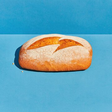 Rustic bread loaf with a floured crust on a vivid cobalt blue background, featuring a sharp shadow for bakery and food packaging layouts