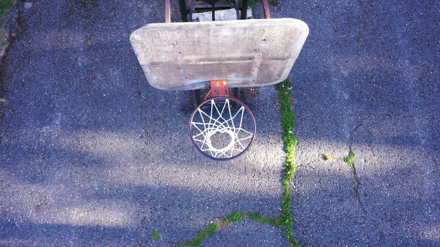 Aerial view of a weathered basketball hoop on an asphalt court with cracks and grass in Latvija.