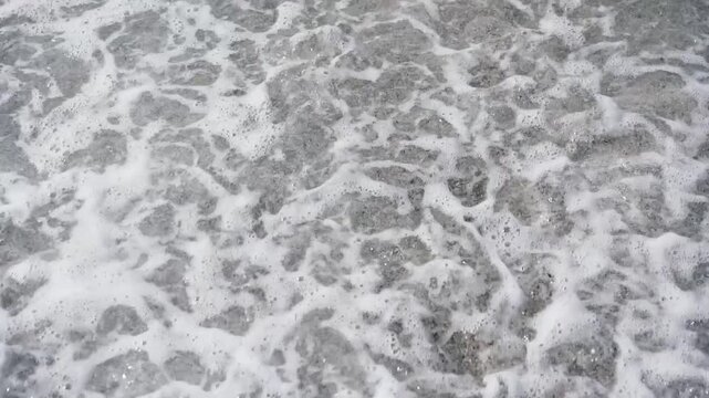 White ocean foam rolling onto beach and receding in slow motion