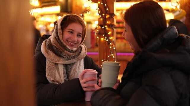 Girls Sweetly Converse, Drinking Hot Holiday Wine At The Bright Christmas Fair In Garland Light