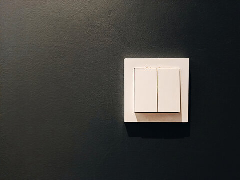 White modern light switch on black wall, interior detail. Close-up view.