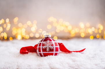 Fototapeta premium A Christmas background featuring red baubles with golden glitter stripes, a star, and ribbon framing wide snowy ground, softly lit by warm twinkling lights with generous copy space.