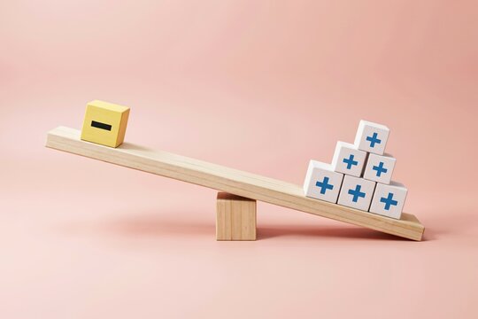 Wooden seesaw balancing a single yellow minus block against a stack of positive blocks on pink background.