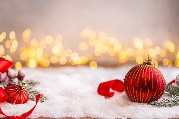 Fototapeta premium A Christmas background featuring red baubles with golden glitter stripes, a star, and ribbon framing wide snowy ground, softly lit by warm twinkling lights with generous copy space.
