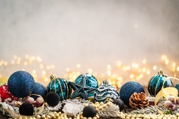 Fototapeta premium A Christmas background featuring navy and teal baubles, a glass star, black velvet balls, and a pinecone resting on golden beads and frosted pine, with twinkling lights and copy space.
