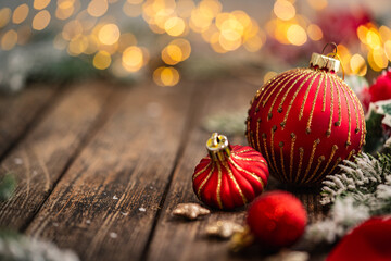 Fototapeta premium A Christmas background featuring red baubles with golden glitter stripes, a star ornament, and frosted pine on a wide rustic wood table, warmly lit with twinkling lights and copy space.