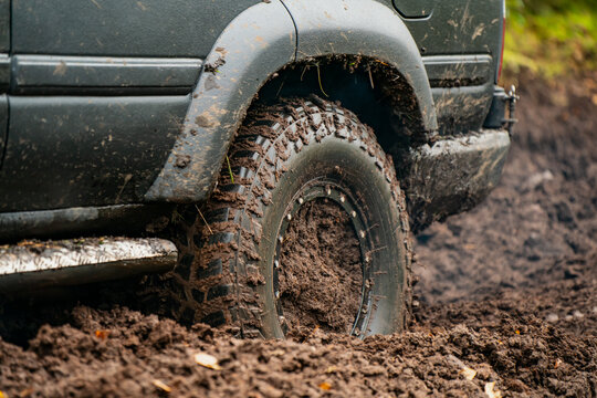 Mud terrain tire on an off-road SUV sunk into a deep trail rut with mud packed around the rim, illustrating traction challenges during recreational 4x4 woodland journeys