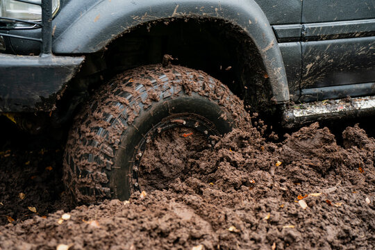 Off-road SUV tire churning thick mud with loose clods around its tread and wheel arch, showing wheelspin and traction challenges during recreational 4x4 trail adventures
