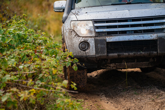 Mud-splashed 4x4 front with a snorkel, illuminated headlamp and treaded tire beside deep forest ruts, showing vehicle equipment used for recreational off-road exploration