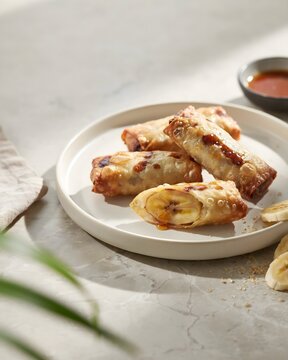 Authentic Filipino Turon Fried Sweet Banana Spring Rolls Drizzled with Caramelized Sugar Served with Banana Slices on White Plate