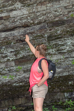 Female hiker touching ancient layered rock wall near Maniavka River, Carpathians, Ukraine. Woman tourist exploring geology in forest near Maniava