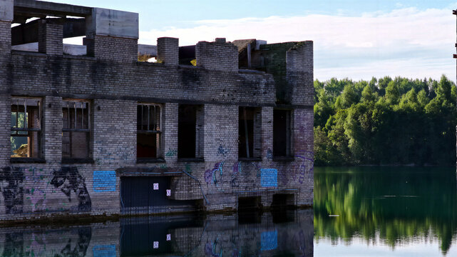Aerial view of the submerged ruins of the Rummu quarry, featuring weathered brick walls, graffiti, and calm turquoise water surrounded by lush green forest in Rummu, Harju County, Estonia.