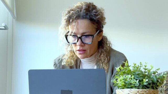 Middle-aged businesswoman with eyeglasses feeling tired and massaging her painful neck while working on a laptop at her desk, suffering from sedentary work health problems and stress