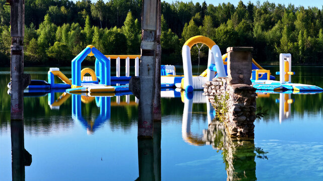 Aerial view of the inflatable water park floating on the clear blue water of Rummu quarry, surrounded by lush green forest and historic stone ruins in Rummu, Harju County, Estonia.