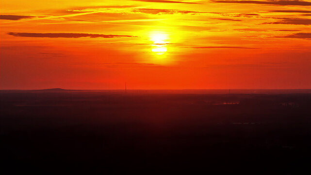 Aerial view of a vibrant sunset casting a warm orange and red glow over the flat horizon and landscape of Latvia.