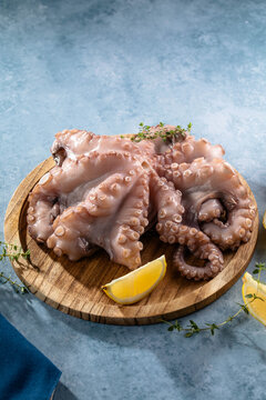 Seafood octopus. Whole fresh raw octopus on wooden board with lemon, herb on blue background, top view.