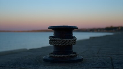 Fototapeta premium Iron mooring bollard with rope at a harbor at dusk, maritime detail