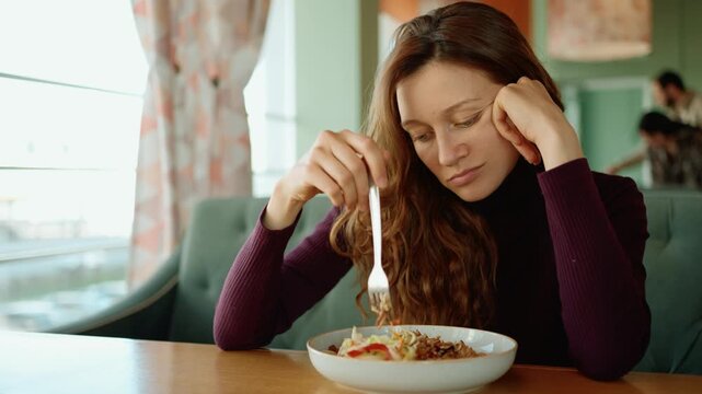 Sad and lonely woman with an eating disorder having no appetite, listlessly picking at her food in a cafe. A visual representation of mental health struggles like depression and anxiety