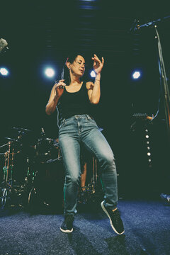 Young woman performs sound check on dark concert stage under blue lights