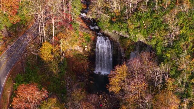 Aerial landscape of mountain waterfall, forest staircase boardwalk and scenic highway. Passing vehicles travel beside colorful autumn woodland.