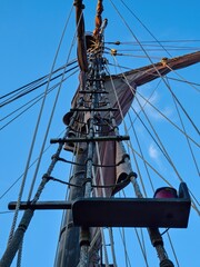 Looking up the wooden mast of an old wooden sailing ship with rigging, ropes and shrouds against a clear blue sky. Vintage maritime vessel and nautical adventure concept. © Igor
