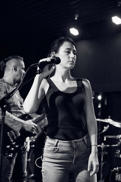 Young woman checks microphone on dark stage during band sound check