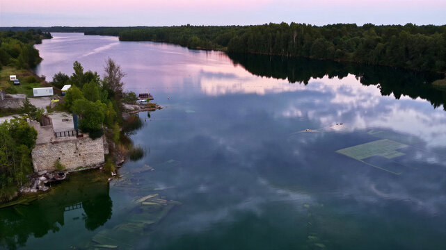 Aerial view of the submerged ruins of Rummu quarry with clear water, surrounding forest, and reflections of the sky at sunset in Rummu, Harju County, Estonia.