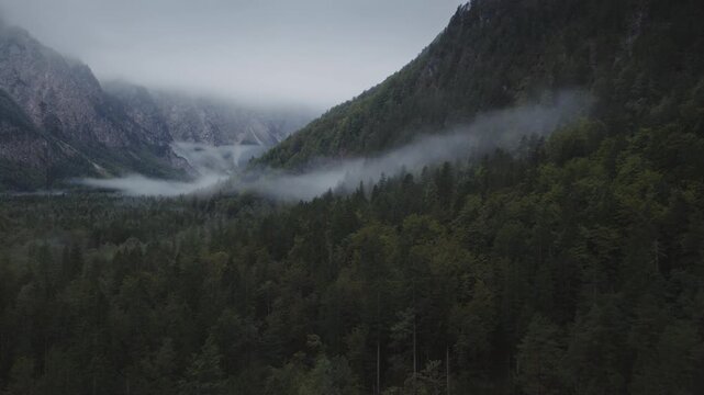 An Aerial of clouds and mist hanging above the woods and mountains in the Logarska Dolina Valley, Slovenia
