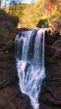 Autumn colored woods around Dry Falls in North Carolina. Scenic waterfall with natural walkway behind rushing water and forest in full fall bloom.