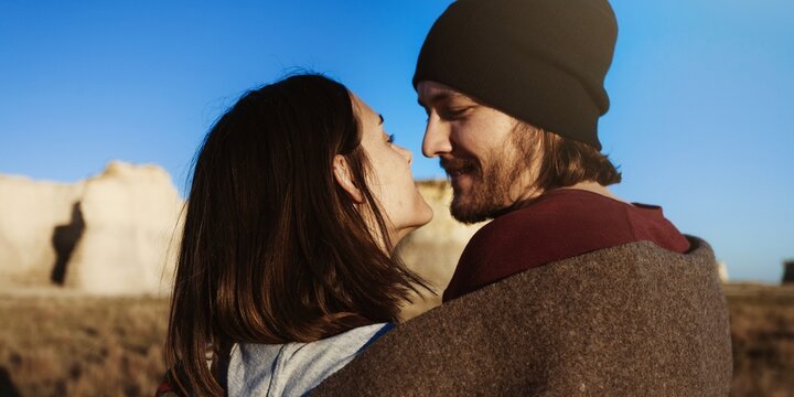 Couple embracing outdoors, smiling under a clear blue sky.