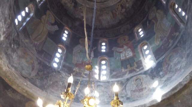 Orthodox dome frescoes and a lit brass chandelier fill the interior of St Naum Church. tilt up shot
