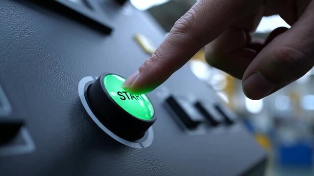 Hand pressing big green start button on industrial machine control panel for factory automation and production launch