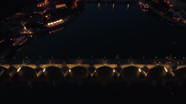 Aerial Tilt Up Above Illuminated Charles Bridge Revealing Historic Prague City at Night Czech Republic