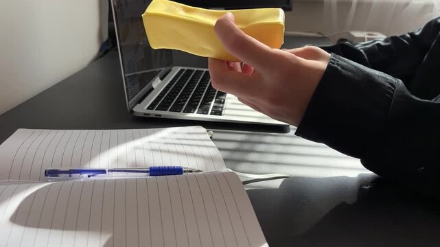 close up of a hand holding and squeezing a funny yellow squishy toy in the shape of a butter stick, blurred laptop on a desk in the background, soft antistress gadget for relaxation and stress relief 