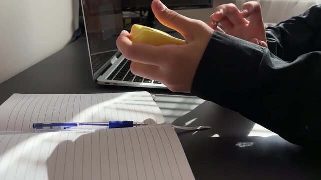 close up of a hand holding and squeezing a funny yellow squishy toy in the shape of a butter stick, blurred laptop on a desk in the background, soft antistress gadget for relaxation and stress relief 