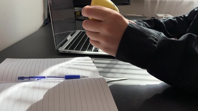 close up of a hand holding and squeezing a funny yellow squishy toy in the shape of a butter stick, blurred laptop on a desk in the background, soft antistress gadget for relaxation and stress relief 