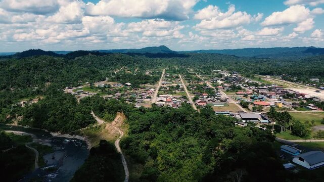 Drone footage looks across a winding river and exposed gravel bars as it passes through dense green rainforest in Ecuador's Oriente. Forested hills extend to the horizon beneath a bright, cloud-filled