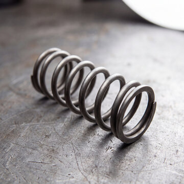 Steel coil spring on a scratched metal workbench