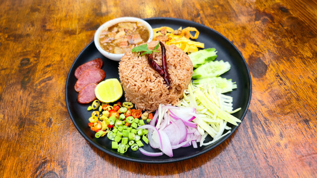 Traditional Thai shrimp paste fried rice served with sausage vegetables mango onion chili lime cucumber and savory side dishes on a black plate restaurant