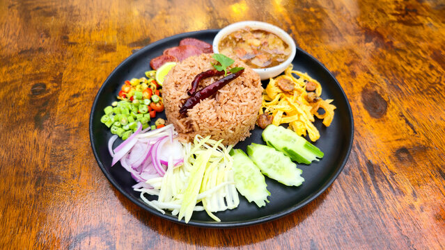 Traditional Thai shrimp paste fried rice served with sausage vegetables mango onion chili lime cucumber and savory side dishes on a black plate restaurant