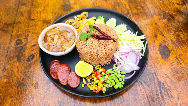 Traditional Thai shrimp paste fried rice served with sausage vegetables mango onion chili lime cucumber and savory side dishes on a black plate restaurant
