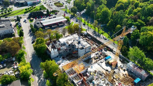 High angle drone shot of a new apartment complex under construction in a green urban area, showing cranes and workers. Suitable for real estate development and urban planning content.