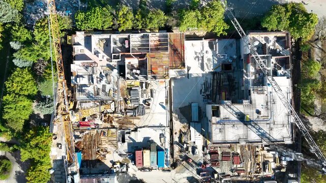 High angle top down perspective of an active construction site featuring tower cranes, concrete structures, and building materials during golden hour. Useful for real estate development and urban plan