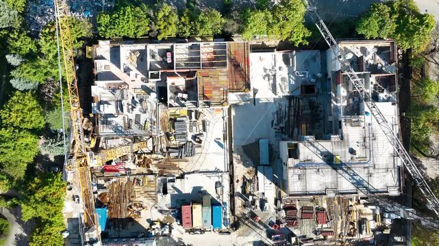 High angle topdown view of a building construction site featuring yellow cranes, concrete foundations, and workers. Ideal for real estate development and urban planning content.