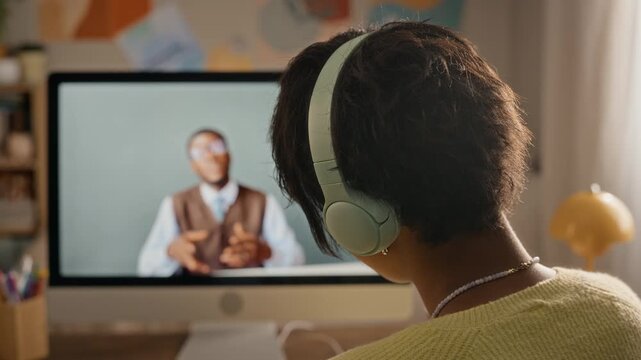 Teenager wearing headphones attending online lesson with African American teacher via computer screen. Footage suitable for edtech promotion, remote tutoring advertising and elearning campaigns